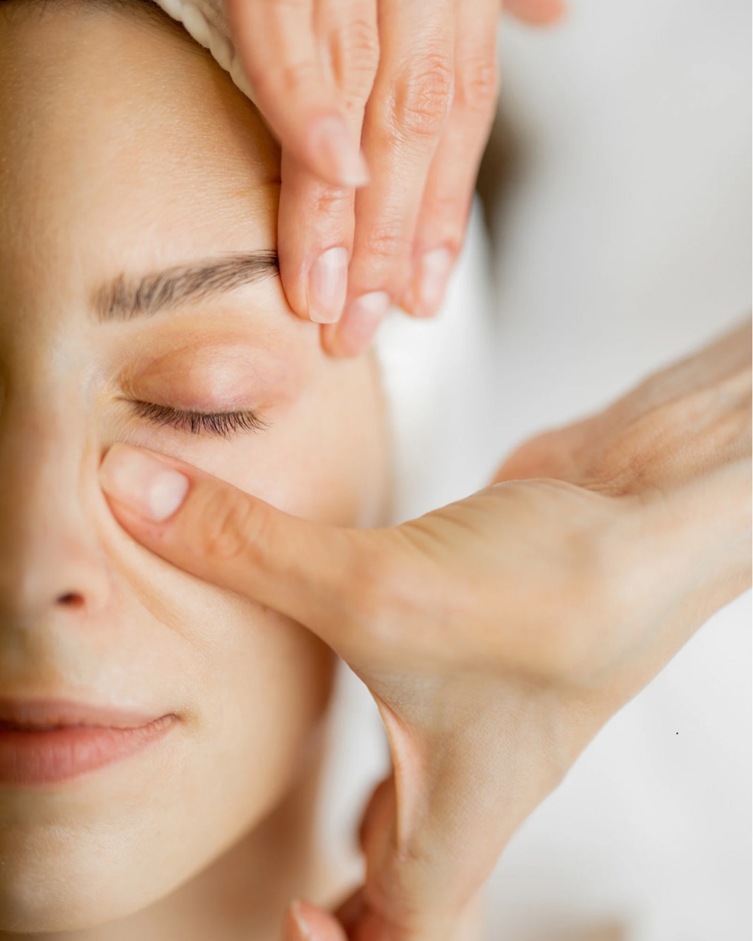 Therapist's hands performing facial massage around a client's closed eye, seen from above